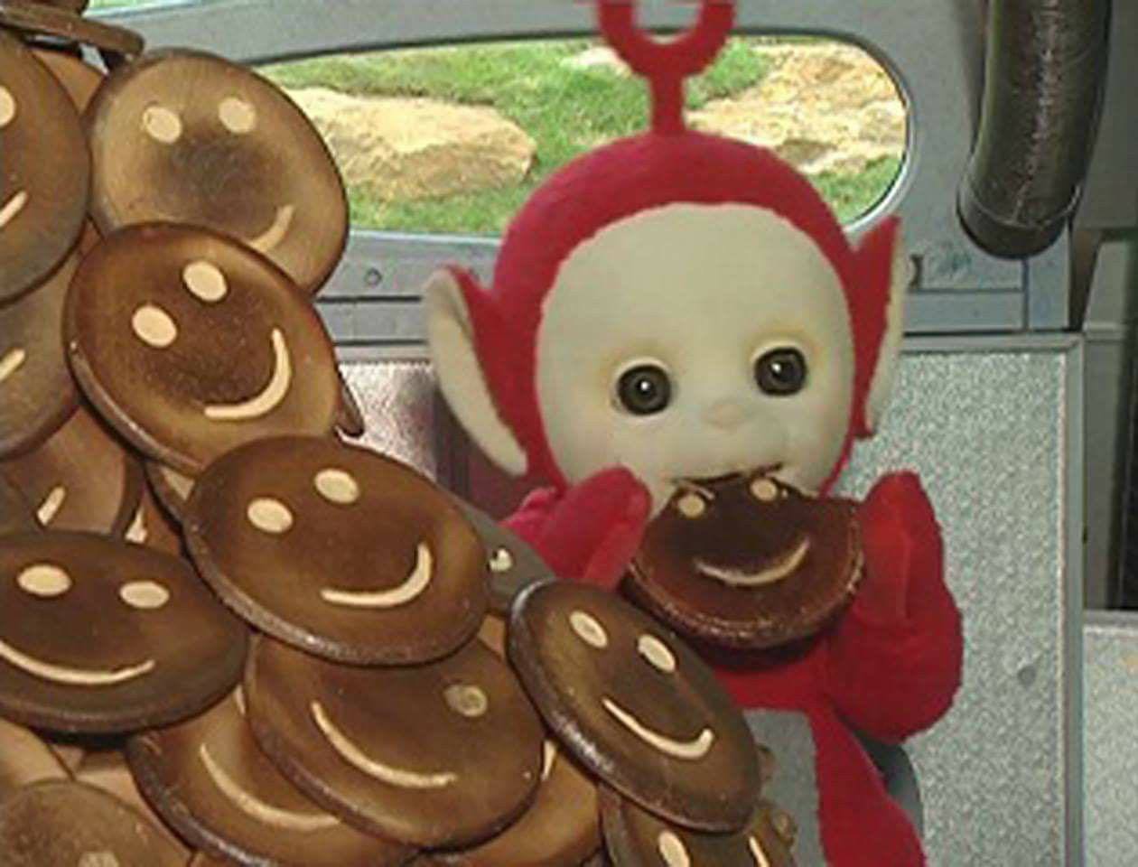 An animated character that resembles a red monkey with large eyes and a round antenna on its head is holding treats with smiley faces.