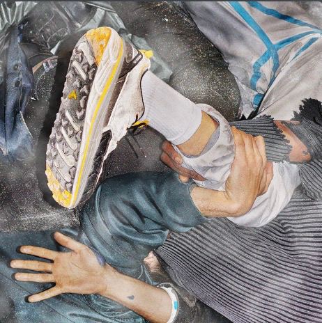 A person is wearing ripped denim pants and checkered yellow and white shoes with the left shoe clearly visible in the foreground. The right hand is placed on a surface, grasping what appears to be a wrinkled structure that might be fabric or some other material.