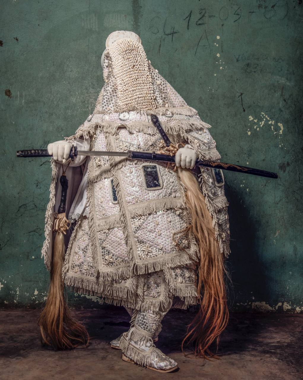 Elaborate costume with intricate beadwork and patterns, head covered in a be