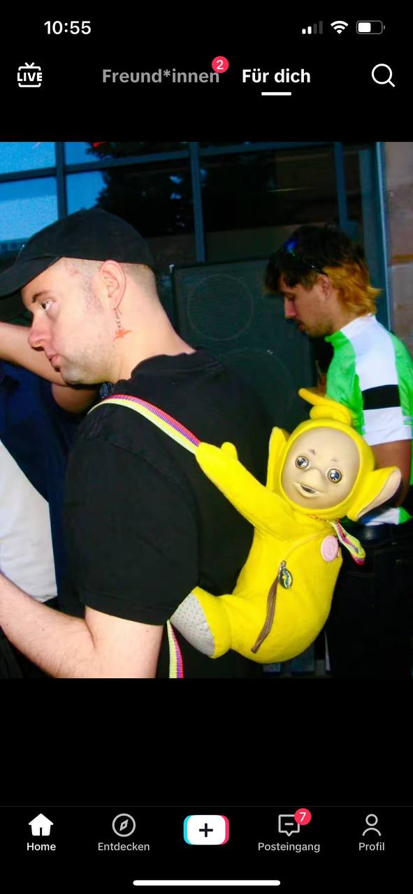 A man is wearing a humorously designed backpack that resembles the character "Teletubby" from the children's
    television series.