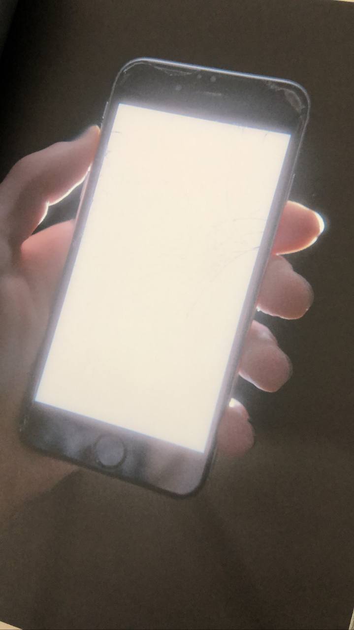 A hand is holding a smartphone with a bright, nearly white screen. The phone appears to be an iPhone, recognizable by the circular home button at the bottom of the screen.