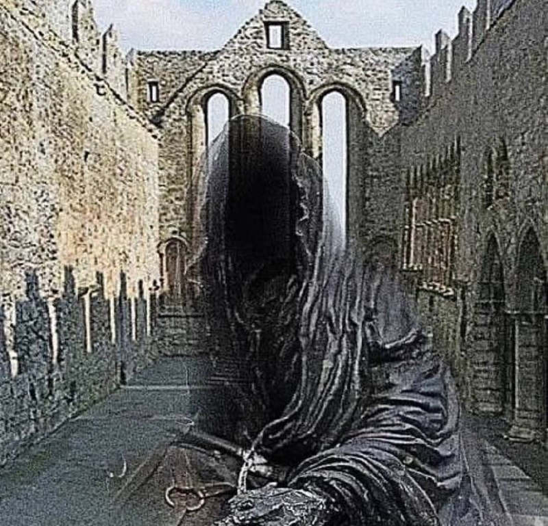 The foreground contains a figure shrouded in black that overlaps onto the scenery of an old, stone-built gothic edifice showing arches and apparent ruins.